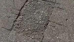 Close-up of a deep crack or permanent gouge in a driveway caused by a heavy roll-off dumpster without wood protection.